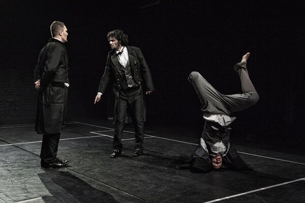 dwóch mężczyzn rozmawia stojąc na przeciw siebie, trzeci stoi na głowie